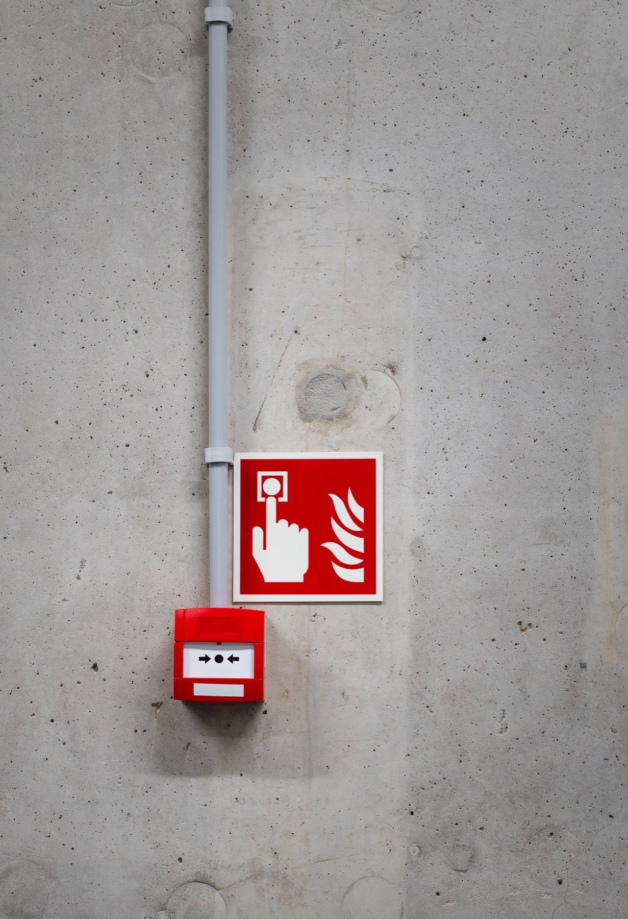 Red manual fire-alarm call point on a concrete wall